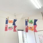 Colorful paper fish garland hanging on a string with clothespins in a classroom or hallway.